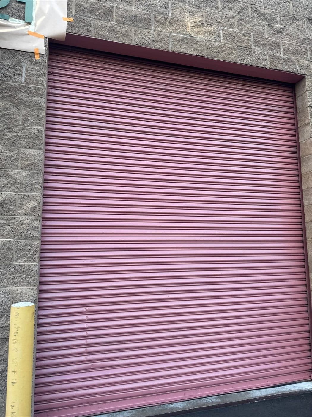 Mauve painted rolling steel overhead door framed by a block warehouse wall.