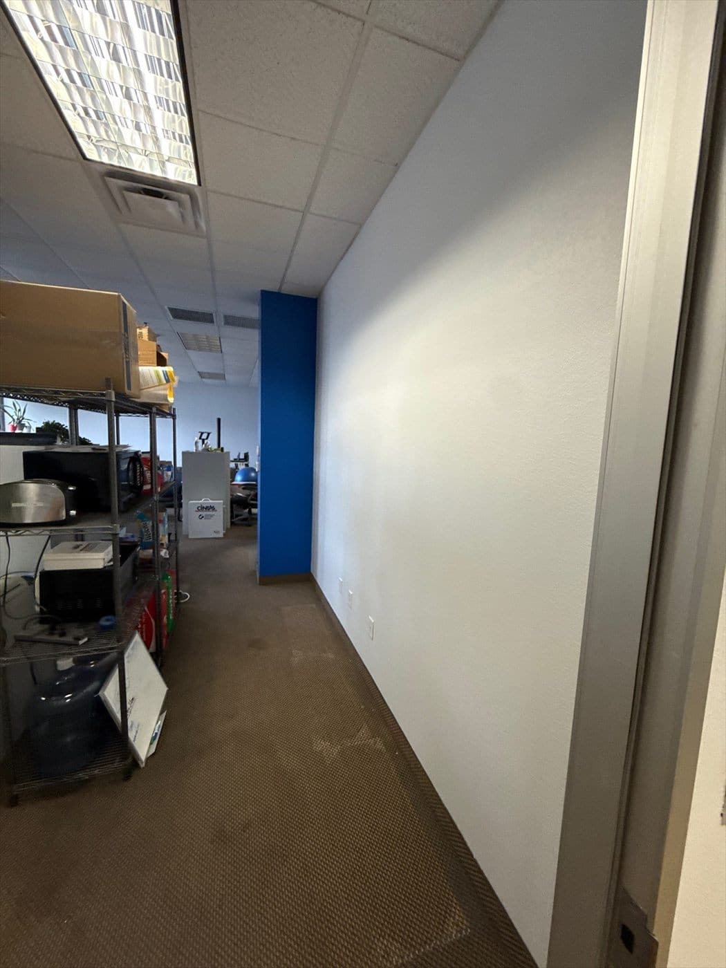 Office hallway with finished white wall and blue accent near storage shelving.