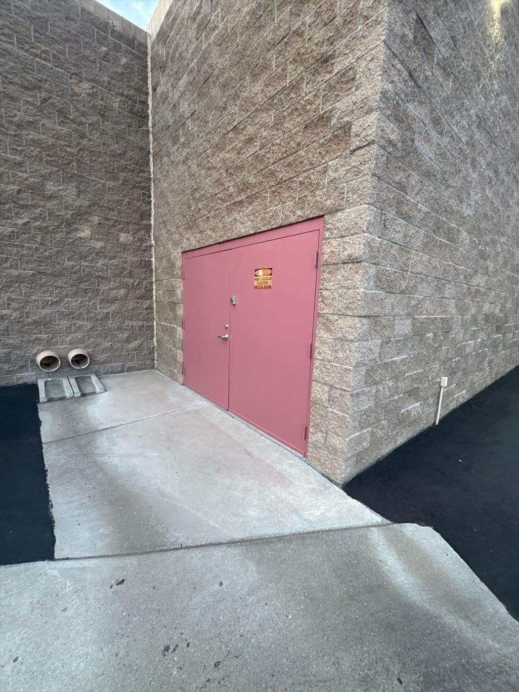 Pink painted double personnel doors in a block wall alcove with exposed conduit.