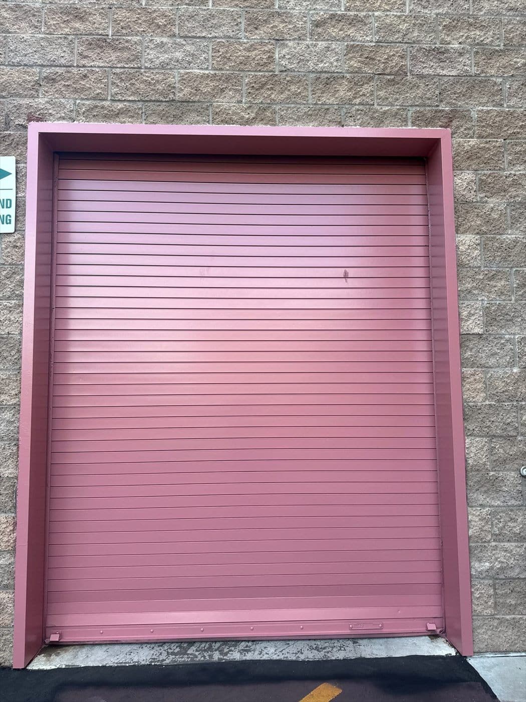 Pink painted rolling overhead door recessed in a block warehouse wall.