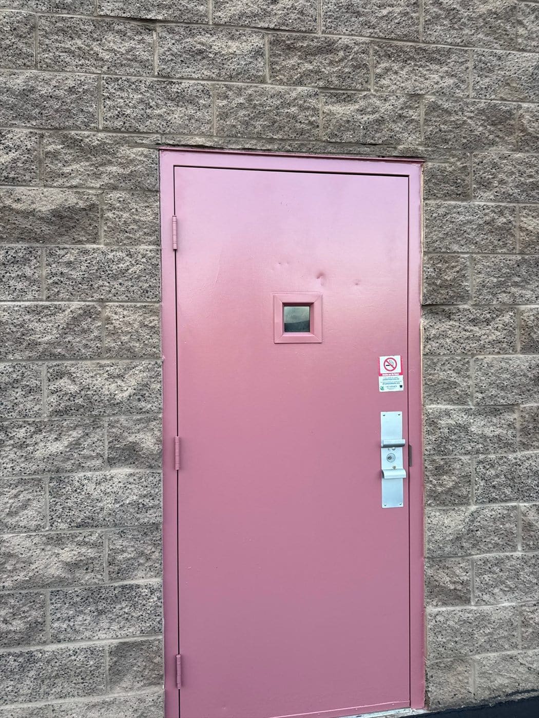 Pink painted steel personnel door with a small window set in a gray block wall.