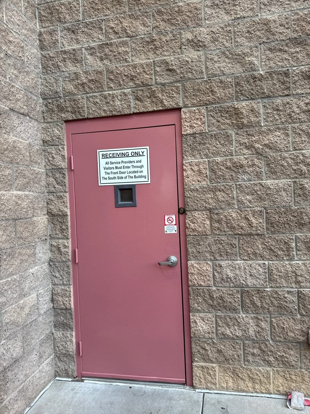 Maroon painted personnel door marked Receiving Only on a tan block wall.