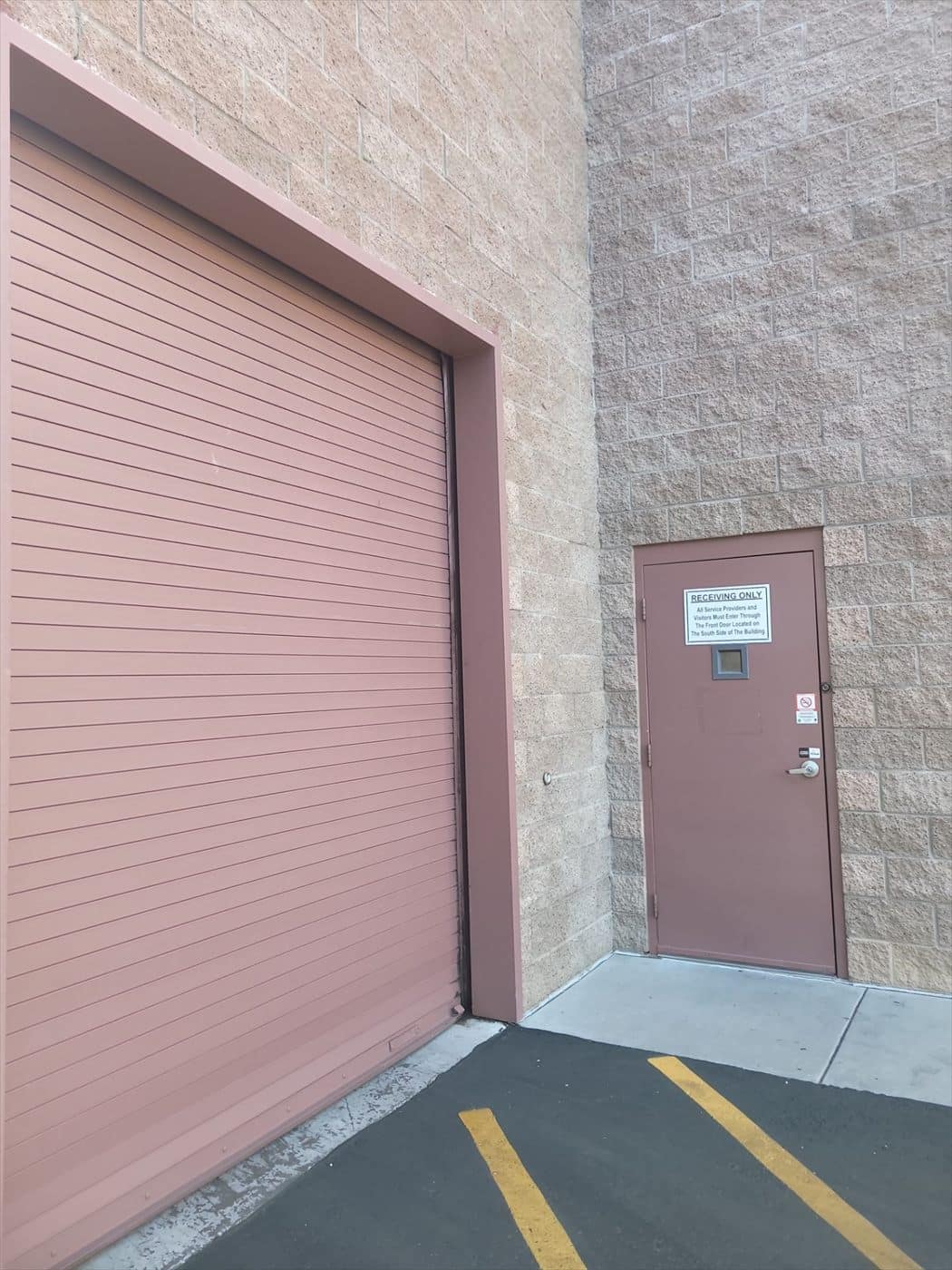 Freshly painted mauve rolling door beside a personnel door with signage in the loading area.