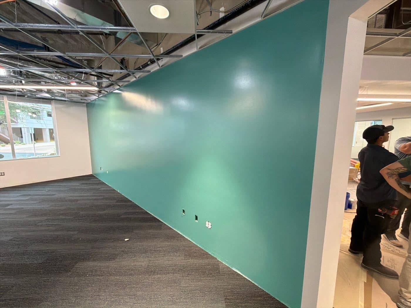 Long teal accent wall in an open area with crew visible in the background.