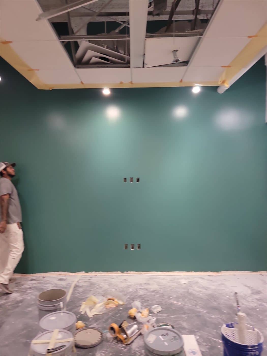 Worker beside a completed teal accent wall with paint supplies on the floor.